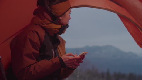 female tourist using smartphone in camping tent in winter