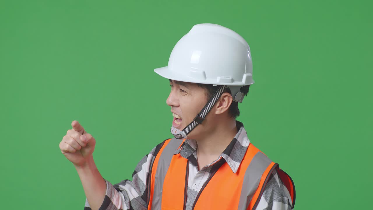 Close Up Side View Of Angry Asian Male Engineer With Safety Helmet Shouting At Someone While Standing In The Green Screen Background Studio