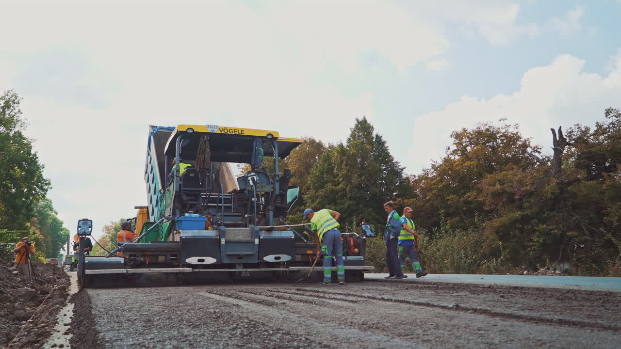 Workers with shovels laying new asphalt. Asphalt road construction. Fresh asphalt is spreading on the road by machine.