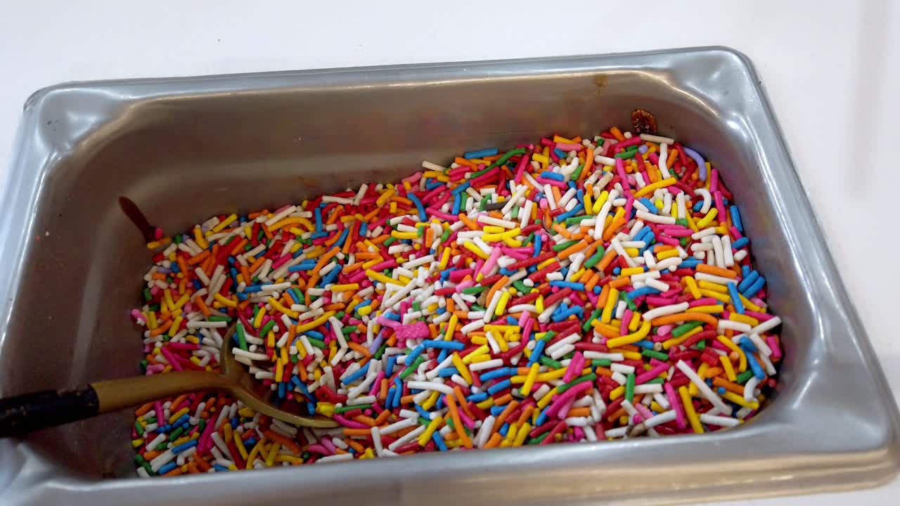 Dettaglio di un mestolo all'interno di un contenitore di codette dolci, utilizzato per decorare gelati e soft serve