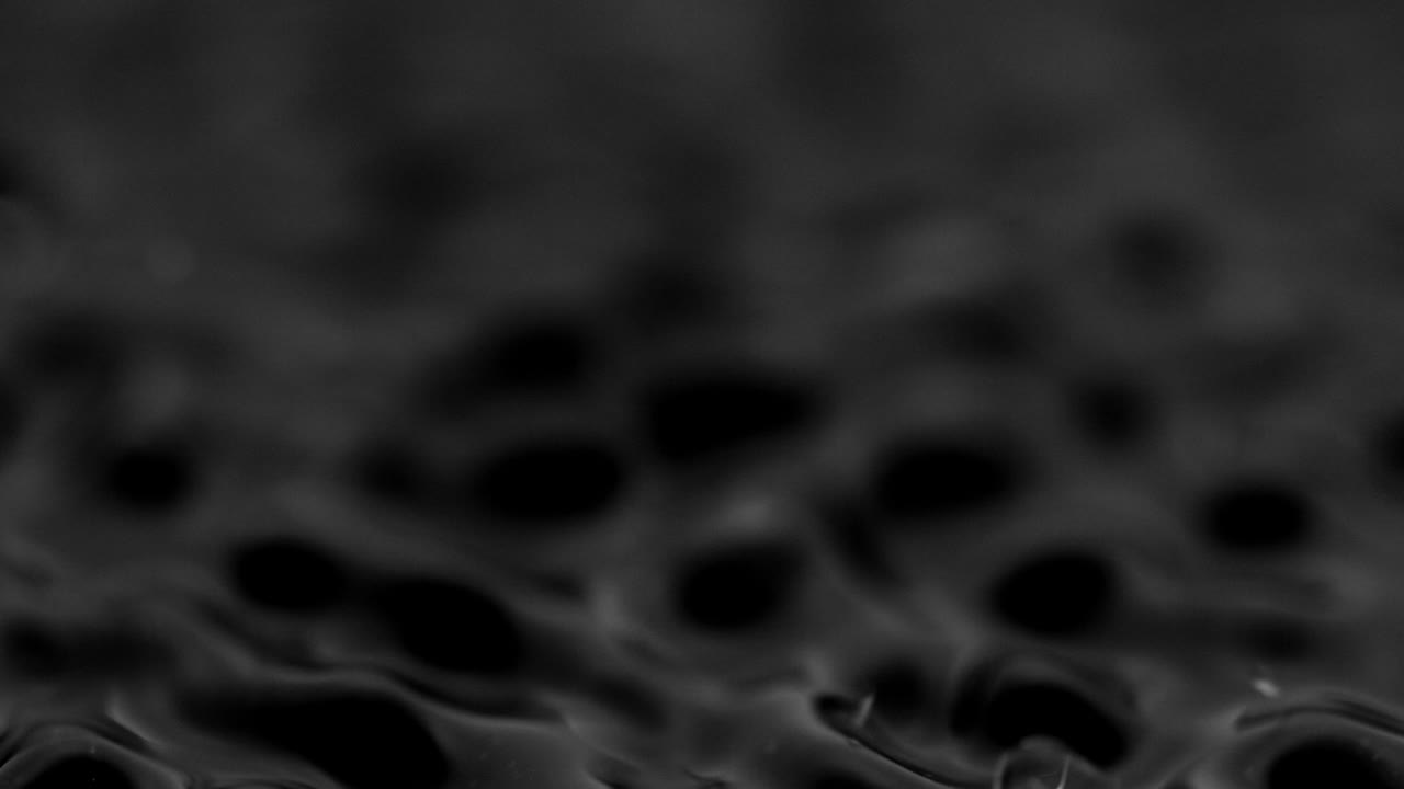 Stænk og dråber på væskens overflade. Abstrakt sort baggrund. Vandvibration. 4K slow motion 100 fps, ProRes 422, 10 bit.