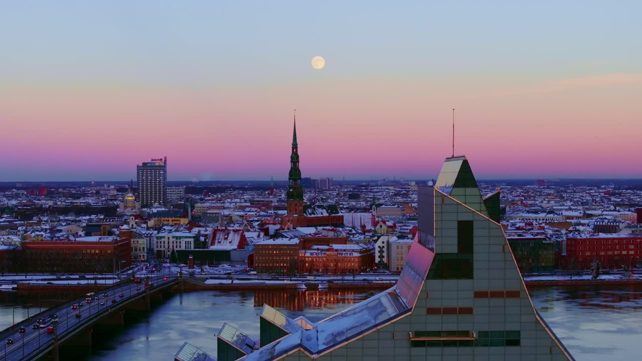Full moon rises over snowy Riga as drone glides backward revealing skyline