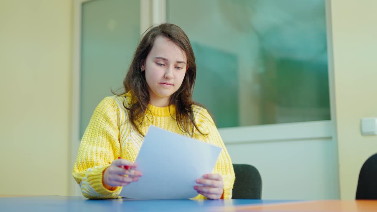 Smiling student studying at school. Beautiful teenage girl holds a paper and throwing it away. Portrait of a school girl sitting in the classroom. Education concept.