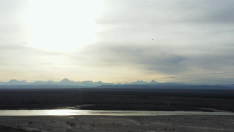 Eagle-circles-in-front-of-river-and-mountains-in-Alaska