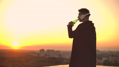 a man drinks beer standing on the roof and contemplates the world. look at the view of the city at sunset from a height. the roof of a skyscraper.