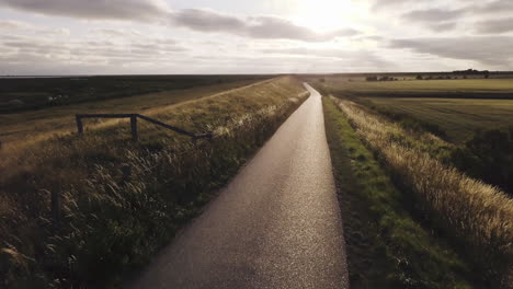 drone flight forward above an empty dyke road, back light, scenic landscape, sunset, sky with scenic clouds