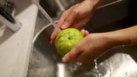 manos lavando una pera bajo agua corriente