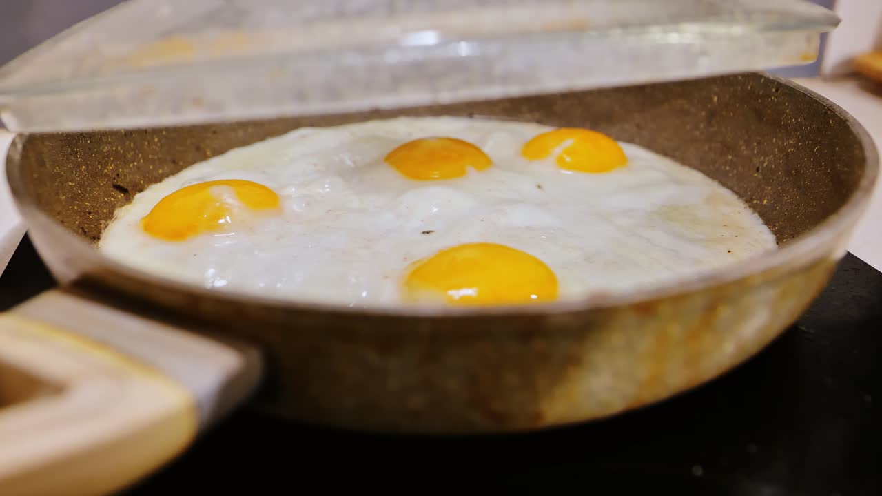 Kuning telur berkilauan melalui tutup saat panas mengukus wajan dengan lembut, momen memasak di dapur