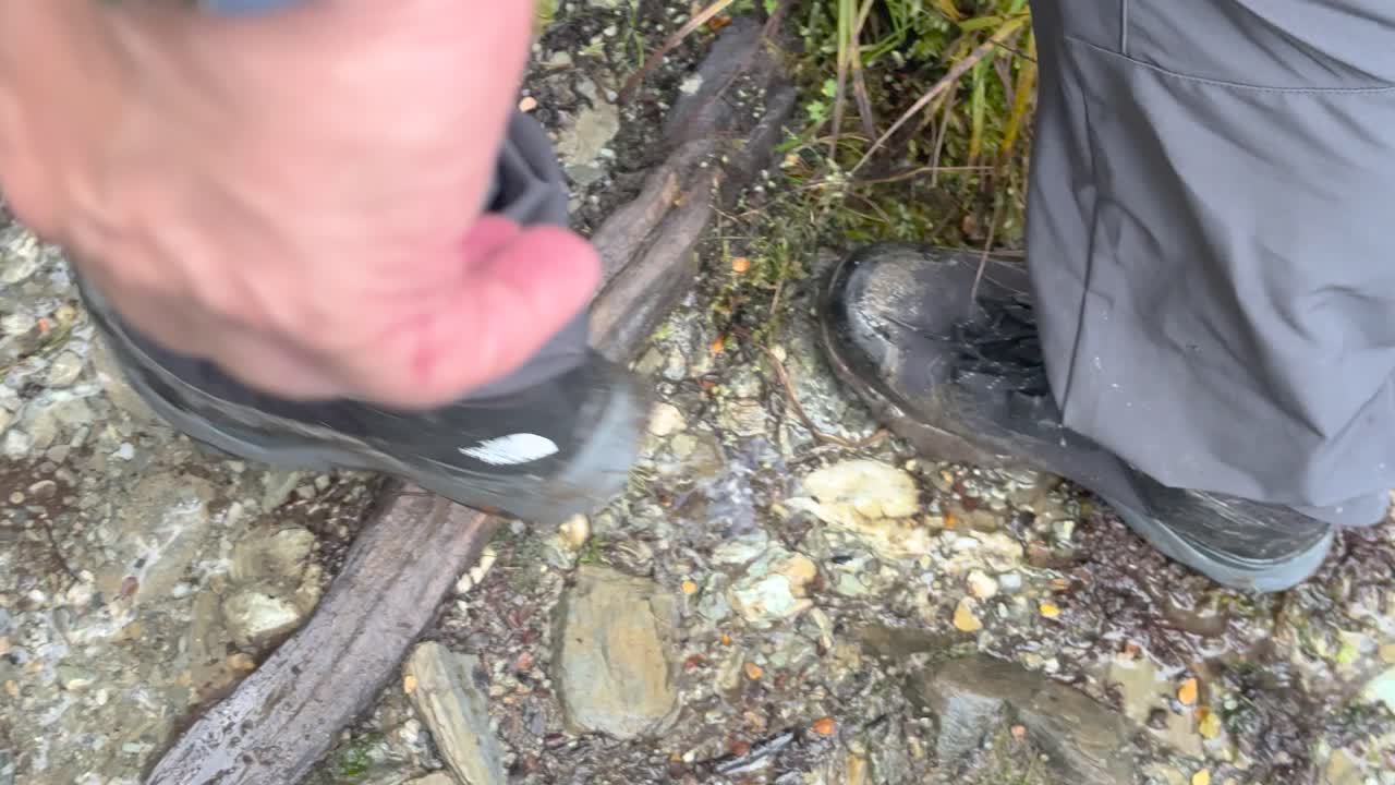 Close-up of hiker’s boots on wet, rocky forest path in natural daylight, handheld shot