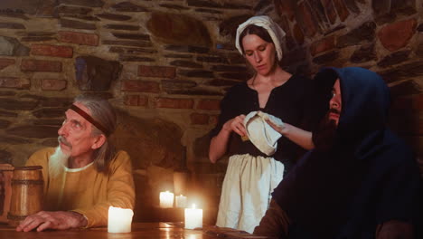 a medieval scene with three people sitting at a table in a tavern