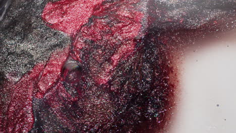macro view of red and black glitter ink slowly spreading across a white surface, forming graphic contrasts