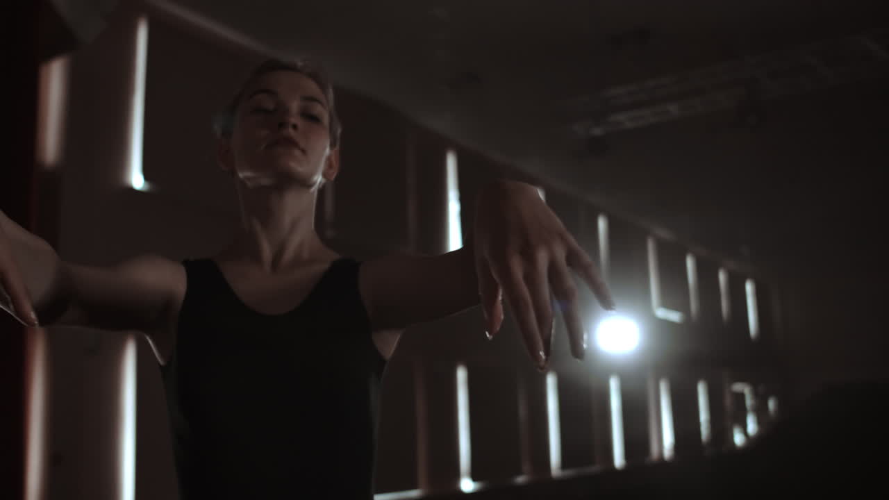 plan medio cámara lenta: una joven bailarina realiza movimientos graciosos en el escenario en un tutu y zapatos de punta en la oscuridad y el humo.