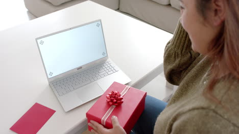 happy plus size biracial woman with gift having laptop video call, copy space on screen, slow motion