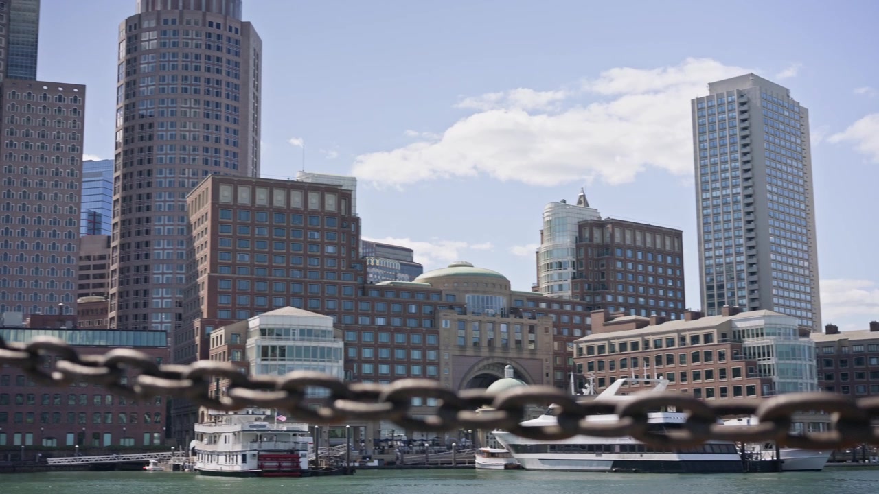 Panoramica cinematografica da destra a sinistra attraverso il porto di Boston che mostra lo skyline del centro di Boston e il lungomare. La luce solare intensa e le acque calme del porto creano uno splendido paesaggio urbano del New England