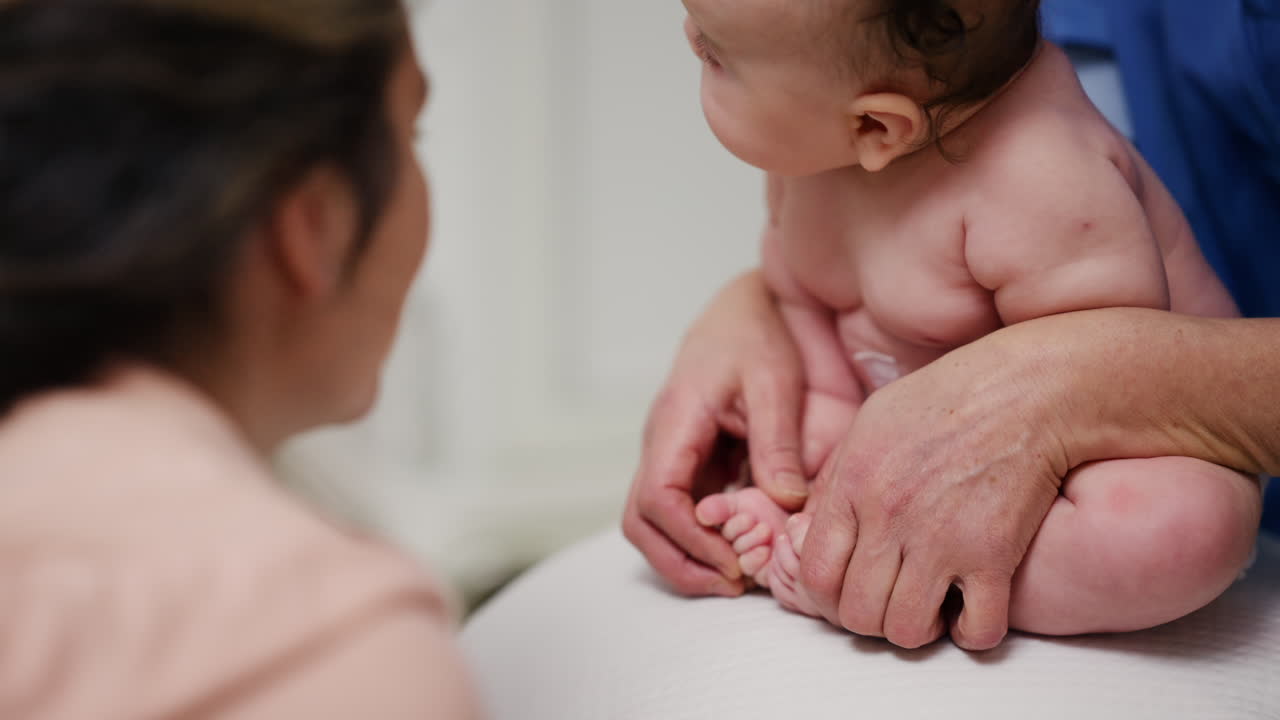 Baby placed on a stability ball while adults support the infant's body