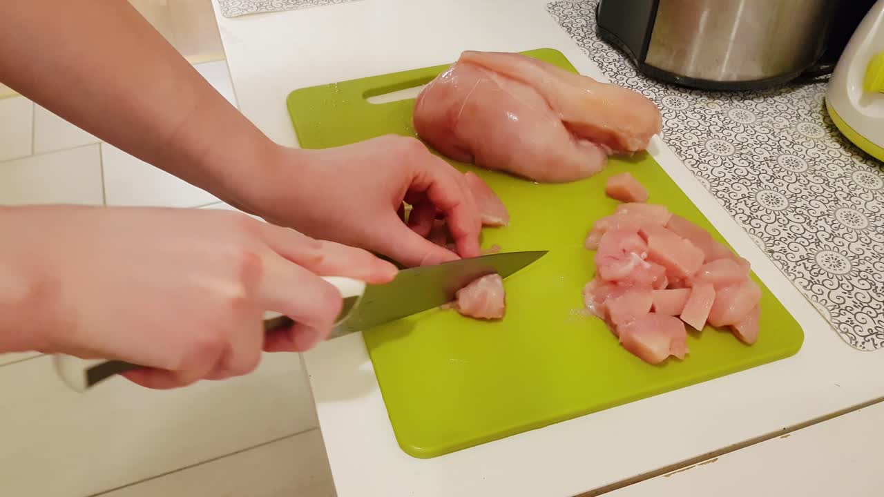 mujer caucásica cocinando y cortando carne de pechuga de pollo cruda