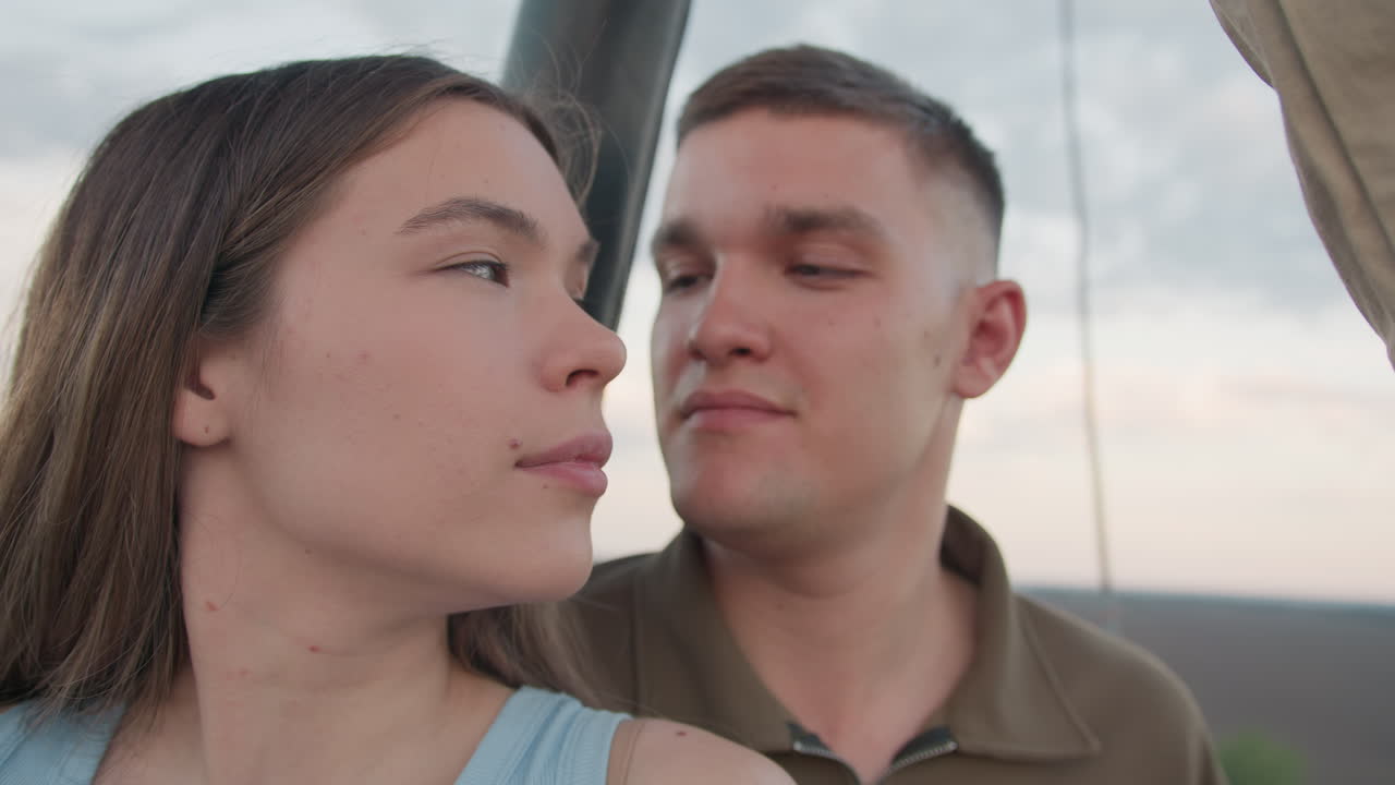 young couple gazes warmly at each other inside hot air balloon basket as colorful envelope floats above capturing romantic adventurous atmosphere high above rolling fields at sunset