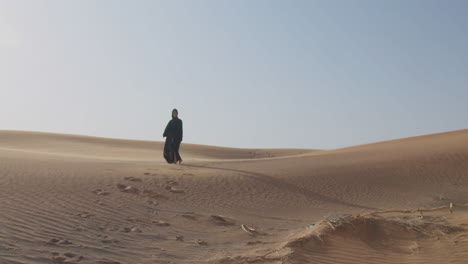 two muslim women wearing traditional dress and hijab walking in a windy desert