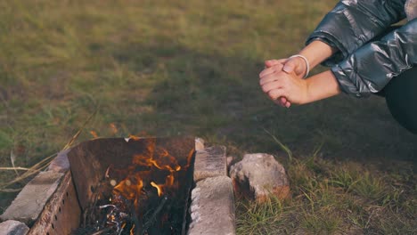 una excursionista calienta las manos en una hoguera en el campamento