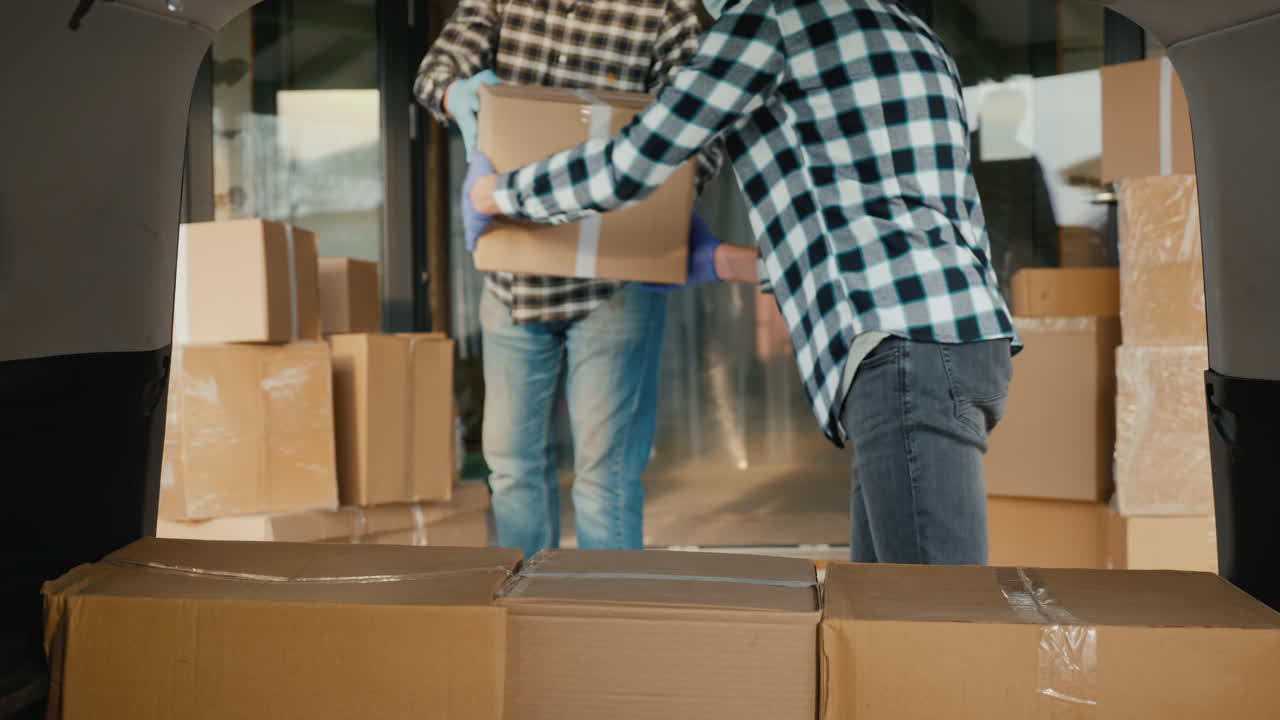 los transportistas con máscaras protectoras cargan cajas de cartón en el maletero de la furgoneta