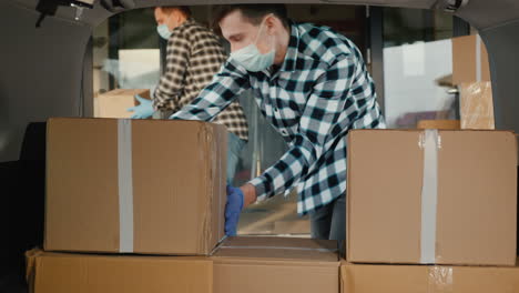 Carriers In Protective Masks Load Cardboard Boxes Into The Trunk Of The Van