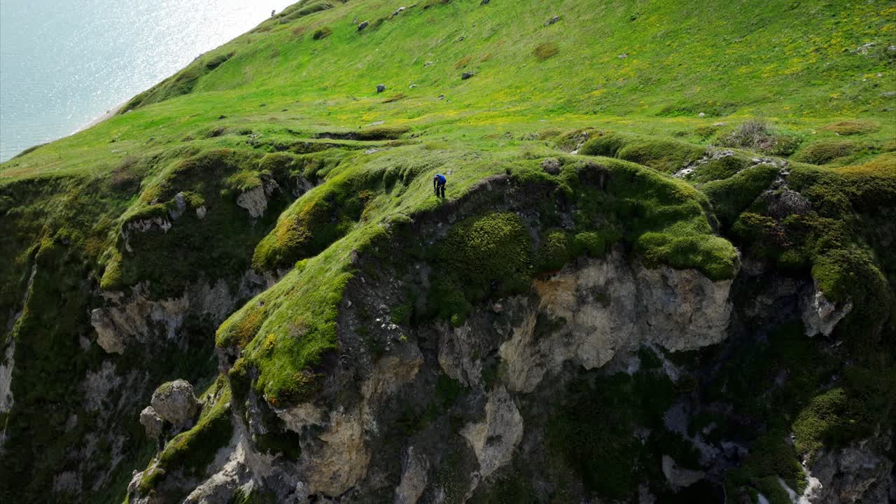 aérea dramática hacia el excursionista en el borde escarpado del acantilado con lago alpino y montañas