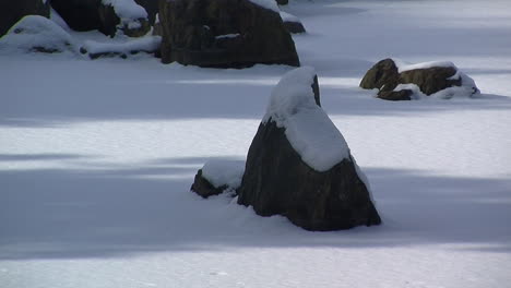 Snow-covered-decorative-rocks-protrude-from-frozen-pond