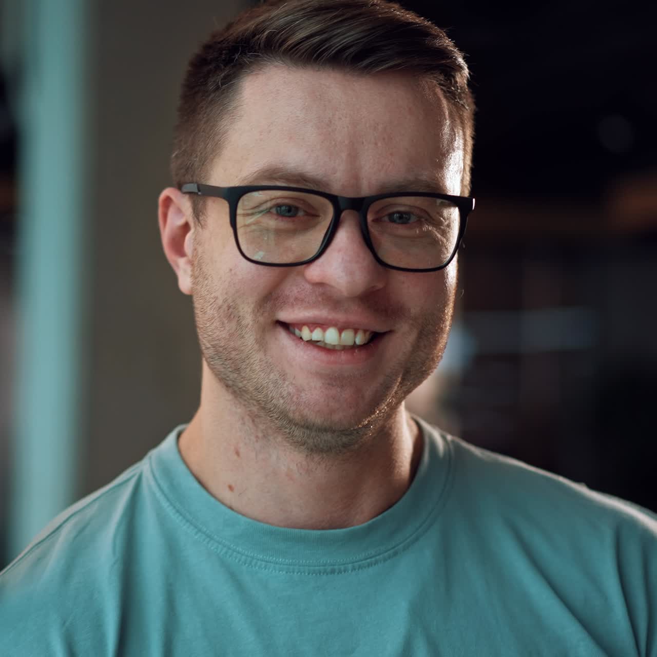 Approaching to a broad-shouldered handsome man in glasses leaning on the window frame. Portrait of a smiling man looking into camera. Close up