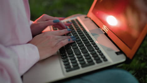 close-up of woman typing on laptop with well-polished nails, warm sunlight reflection on keyboard, and soft bokeh light effect in the background