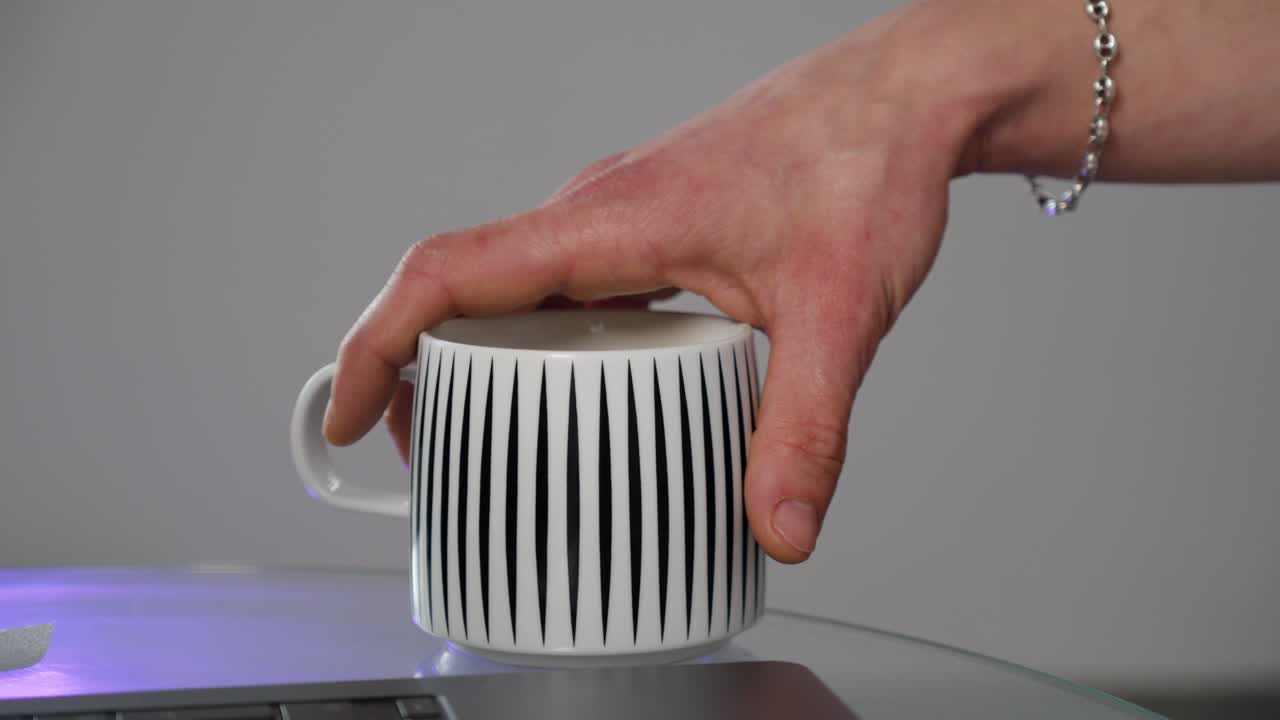Close-up of a hand picking up a modern coffee mug beside a laptop, representing daily routine, home office life, or creative work moments.