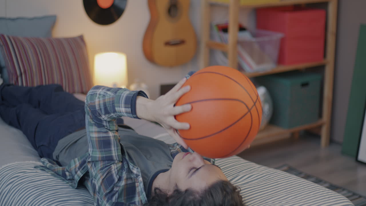 Teenage boy playing basketball on his bed