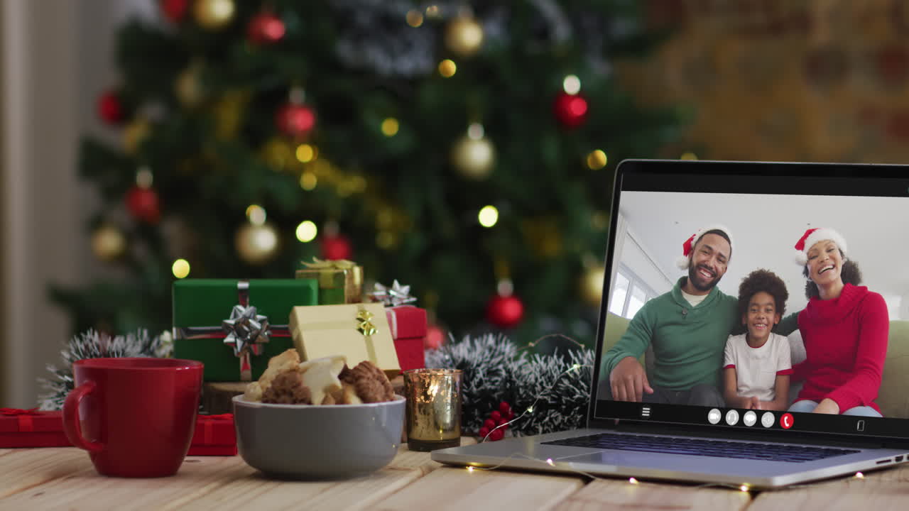 familia feliz usando sombreros de santa en una videollamada en una computadora portátil, con decoraciones de navidad y árbol