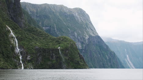 Spectacular-point-of-view-from-a-boat,-gazing-at-misty-waterfalls-cascading-down-steep-cliffs-in-the-Milford-Sound