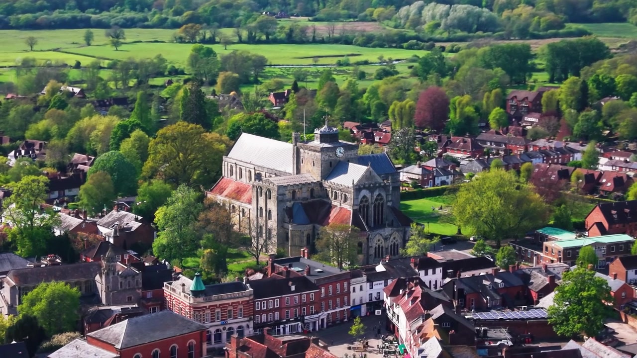 Riprese aeree con drone dell'Abbazia di Romsey nell'Hampshire, che mostrano la storica chiesa abbaziale, i tetti della città, alberi, spazi verdi e la campagna circostante in una giornata di sole. Utile per il patrimonio britannico