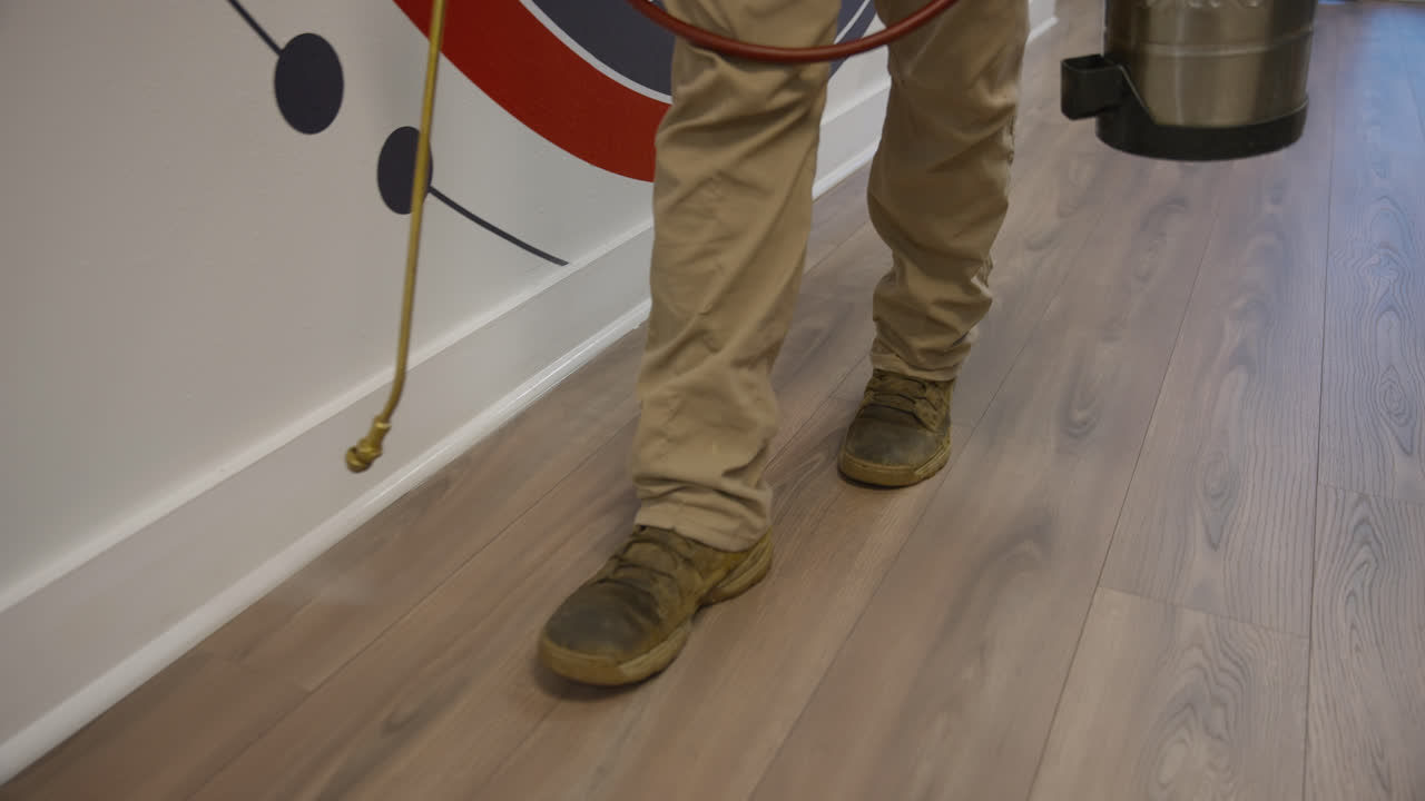 Close low details of technician applying pesticide along office baseboards on wood flooring