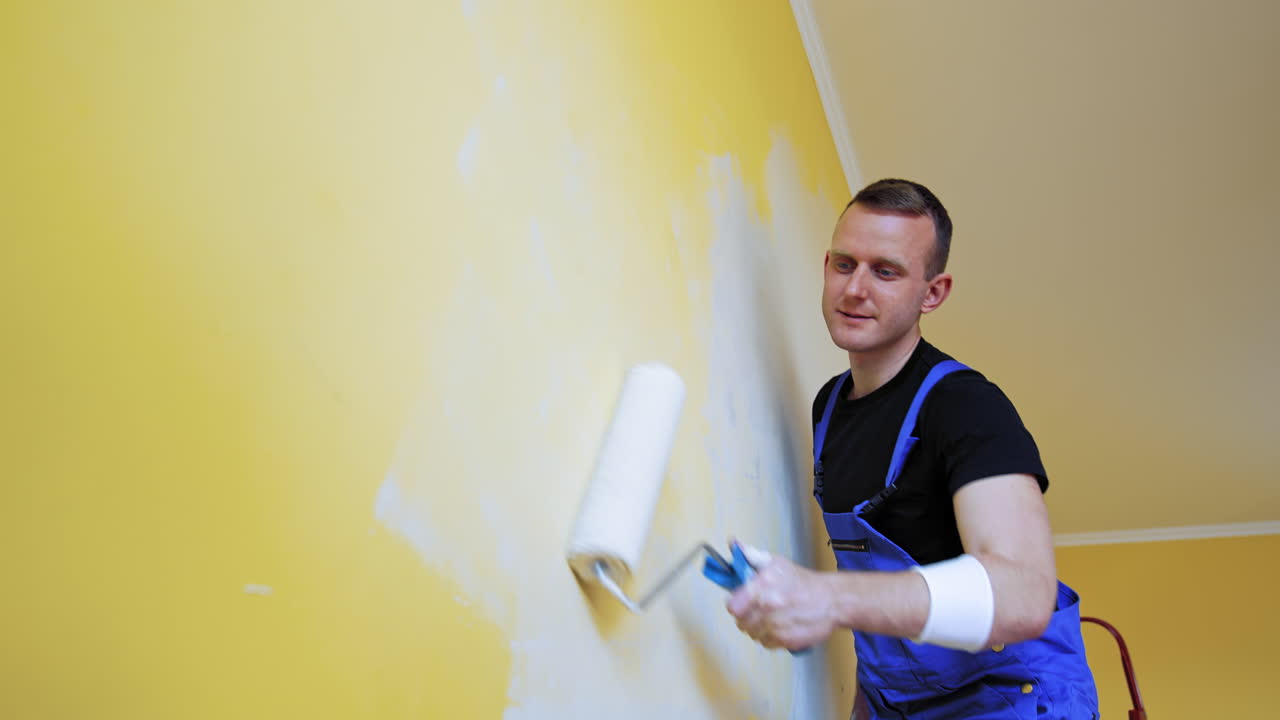 Attractive painter doing new interior of wall. Cheerful man working with paintings.