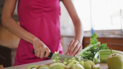 Happy-mixed-race-woman-cutting-vegetables-in-kitchen