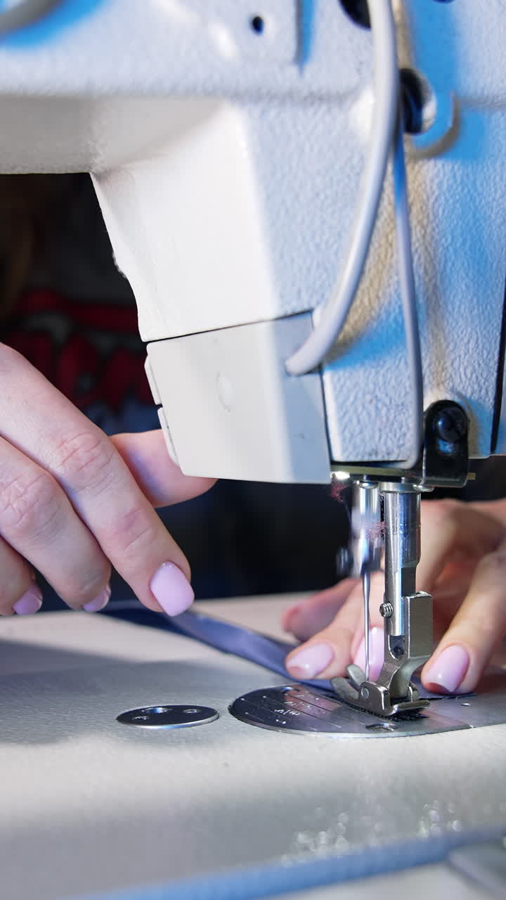 Process of sewing fabric on a sewing machine. Tailor working with sewing machine at workshop. Female's hand pushing material through sewing machine. Vertical video