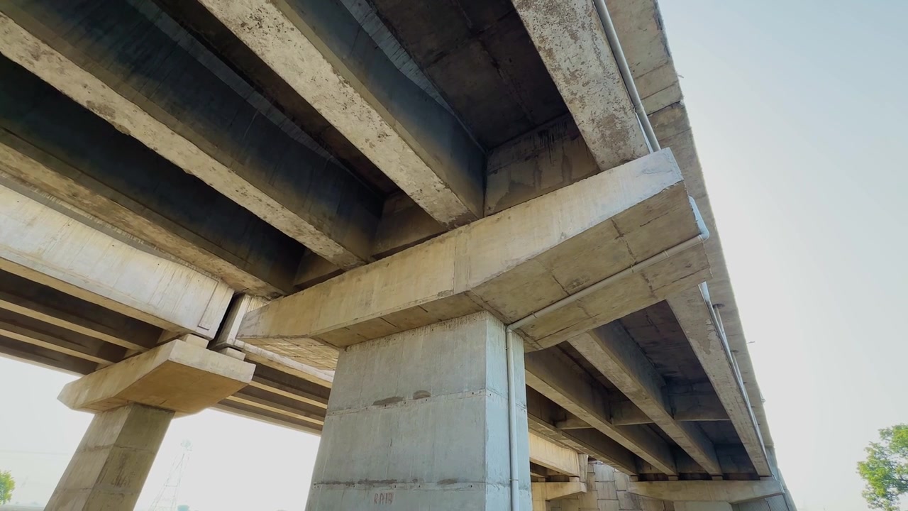 Panning shot beneath a reinforced concrete bridge showing pier caps girders support columns and structural elements of a modern elevated roadway transportation infrastructure project