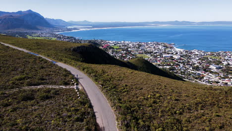 Ciclista-En-Mtb-Paseos-Disco-Giratorio-Carretera-De-Montaña-Con-Vistas-A-Walker-Bay,-Hermanus