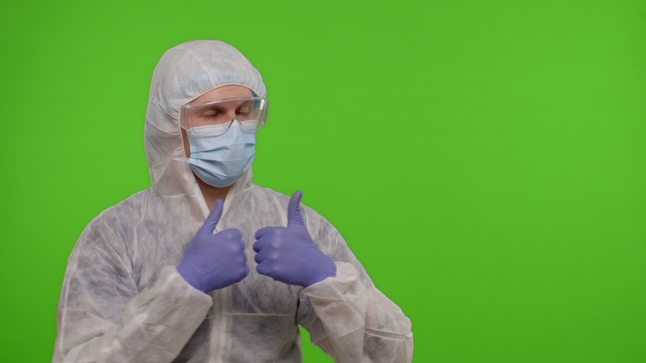 Medical doctor in protective PPE suit pointing at right on blank space on chroma key background