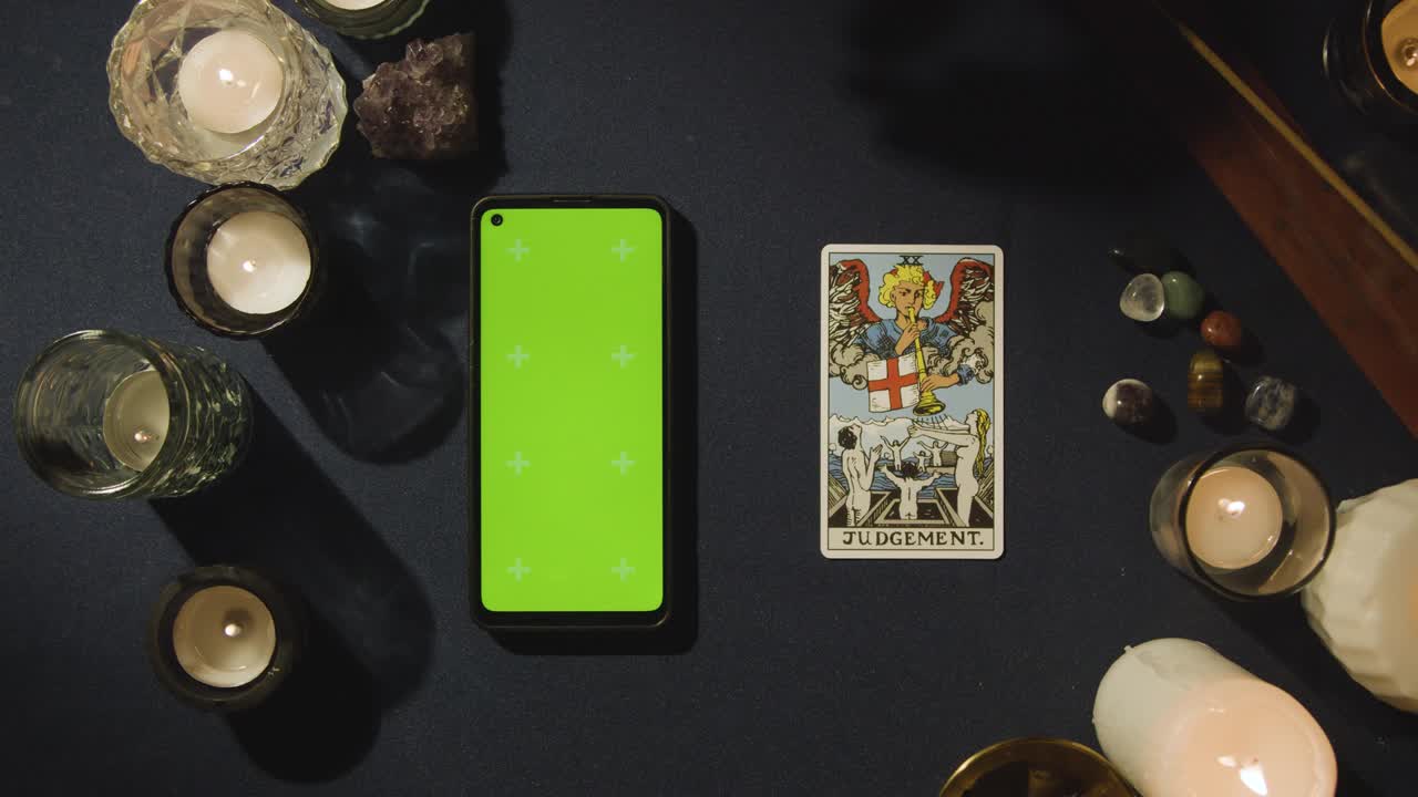 disparo aéreo de una persona que da lectura de tarot con pantalla verde teléfono móvil al lado de la tarjeta de juicio en la mesa
