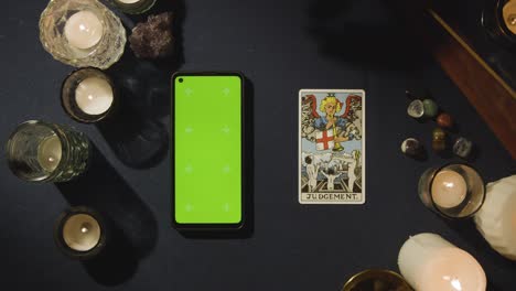 overhead shot of person giving tarot card reading with green screen mobile phone next to judgement card on table