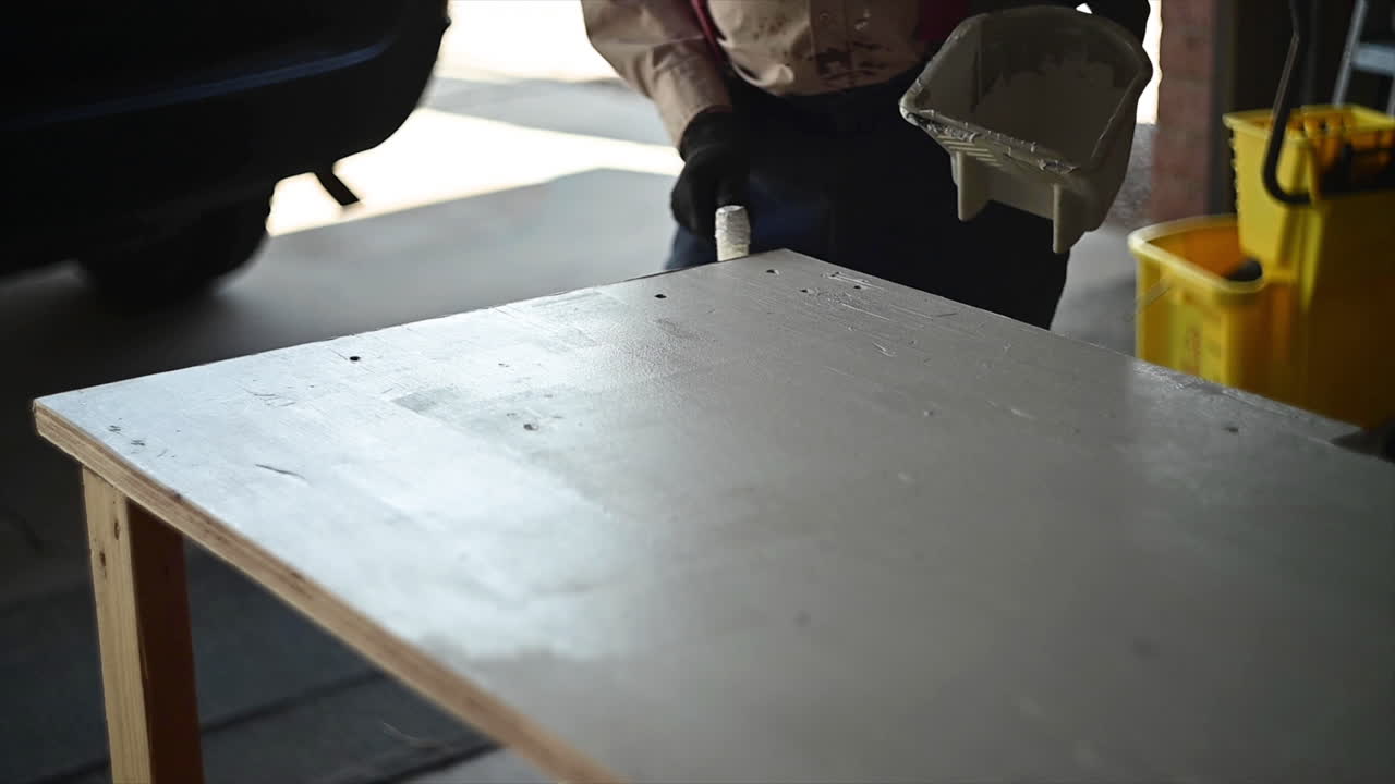 Uomo nel garage che dipinge un tavolo di legno bianco