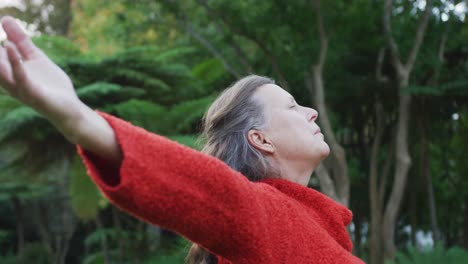 mujer caucásica mayor feliz de pie estirándose en el jardín, relajándose con los ojos cerrados