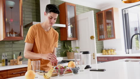 Hombre-Birracial-Feliz-Preparando-Batido-De-Fruta-Saludable-Con-Licuadora-En-La-Cocina,-Espacio-Para-Copiar,-Cámara-Lenta