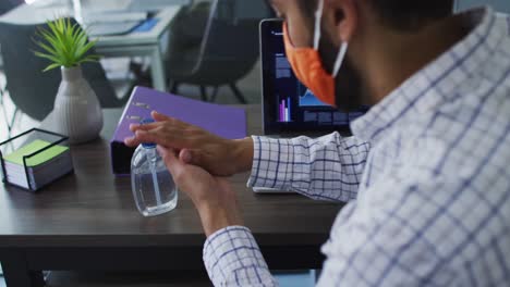 Middle-eastern-man-wearing-face-mask-using-hands-sanitizer-at-modern-office