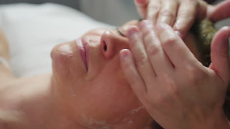 specialist gently rubs individual face with massage gel on hands, smoothing product across cheeks and forehead, creating calming spa experience with soft touch and fluid motion