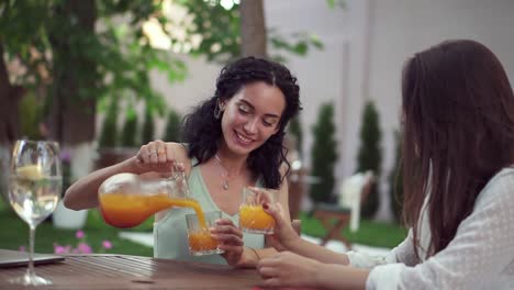 personas, comunicación y concepto de amistad - mujeres europeas jóvenes sonrientes bebiendo jugo de naranja y hablando en un café al aire libre