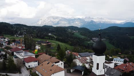 drone shot flying by the church in oberbozen, italy to reveal the looming mountainous landscape